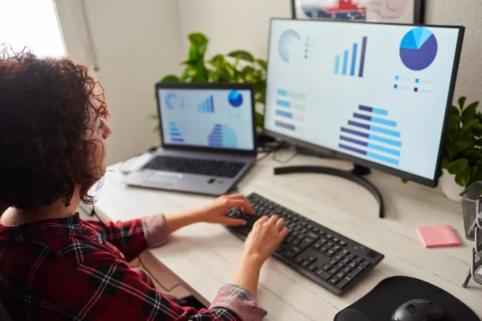 Pessoa analisa gráficos de produtividade em dois monitores como parte do controle de projetos