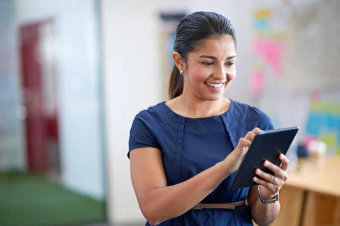 Profissional sorridente usando um tablet para revisar tarefas e cronogramas de projeto aplicando o timeboxing estratégico.
