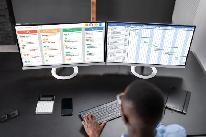 Profissional observando dois monitores com quadros Kanban e gráfico de Gantt, representando a aplicação do timeboxing no FlowUp.