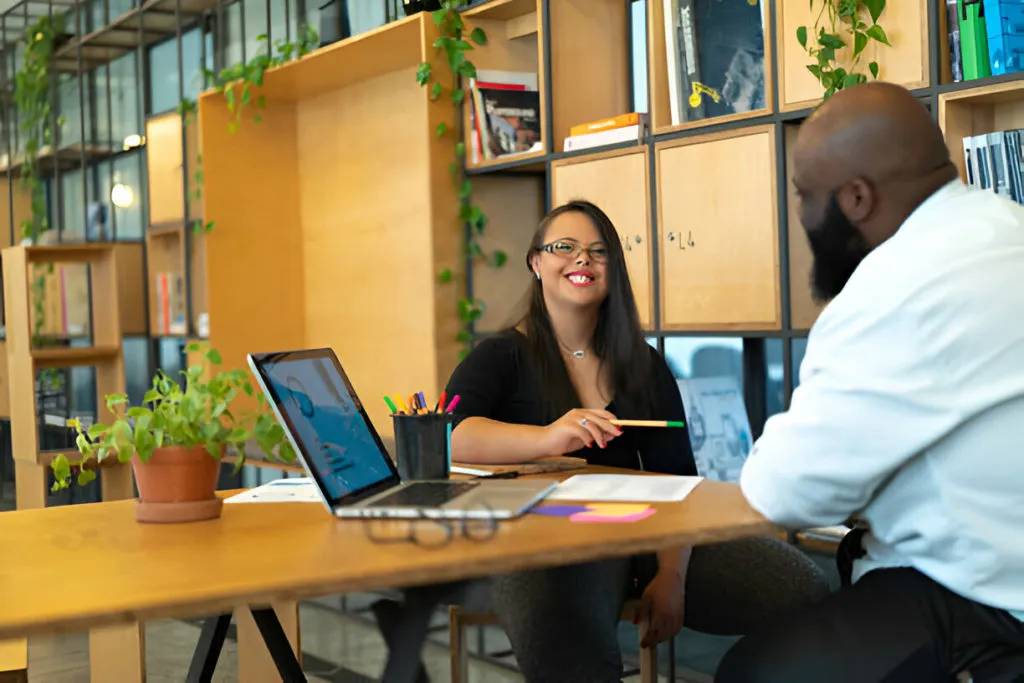 Duas pessoas discutindo estratégias de trabalho em um ambiente moderno com notebook e anotações visíveis