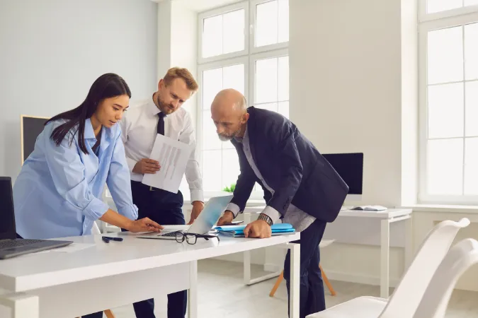 Três profissionais revisando documentos e dados em um notebook, representando o uso de um ERP online para tomada de decisão estratégica