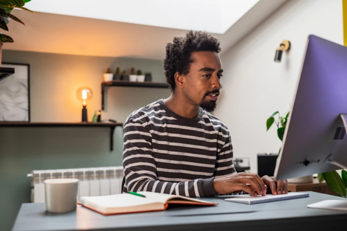 Homem trabalhando no computador com caderno aberto, representando foco e organização para evitar a procrastinação.