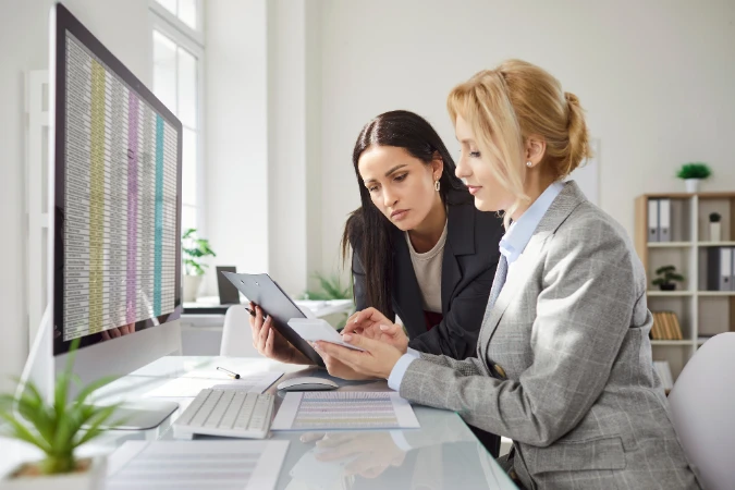 Duas gestoras analisando relatórios e revisando cronogramas inteligentes para manter o projeto no prazo.