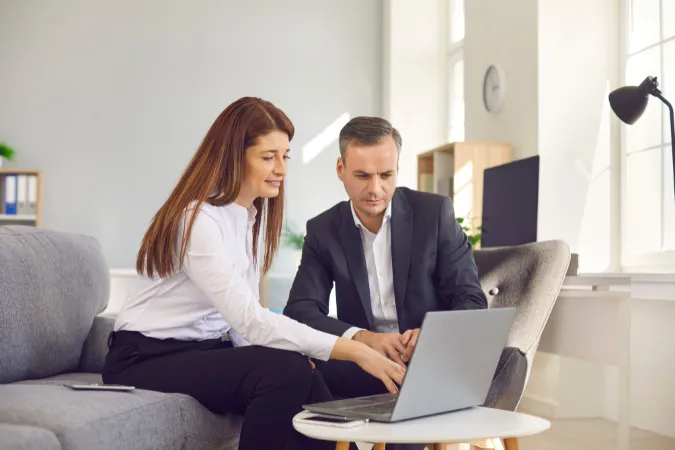 Duas pessoas em ambiente corporativo analisando dados no notebook, simbolizando revisão de processos e indicadores de performance de projetos