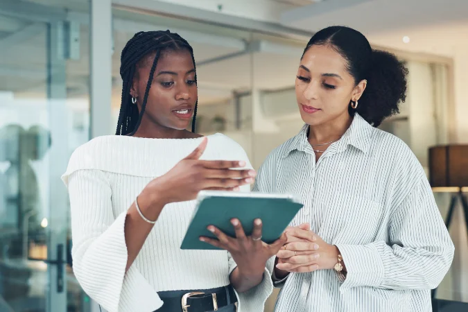 Duas profissionais analisando informações em tablet durante reunião de alinhamento com stakeholders