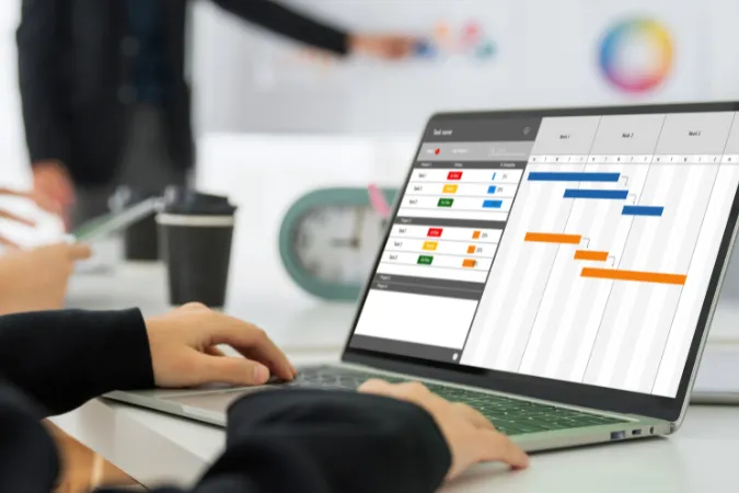 Pessoa usando laptop com gráfico de Gantt e painel de tarefas em um sistema de gestão de projetos.