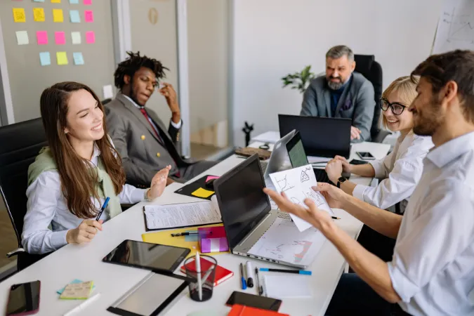 Grupo de trabalho em reunião com notebooks e relatórios visuais sobre a mesa.
