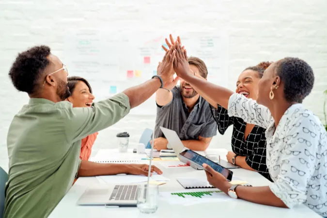 Grupo de profissionais de arquitetura e engenharia comemorando em uma reunião, após alcançar resultados planejados com o uso de metas SMART e ferramentas de gestão.