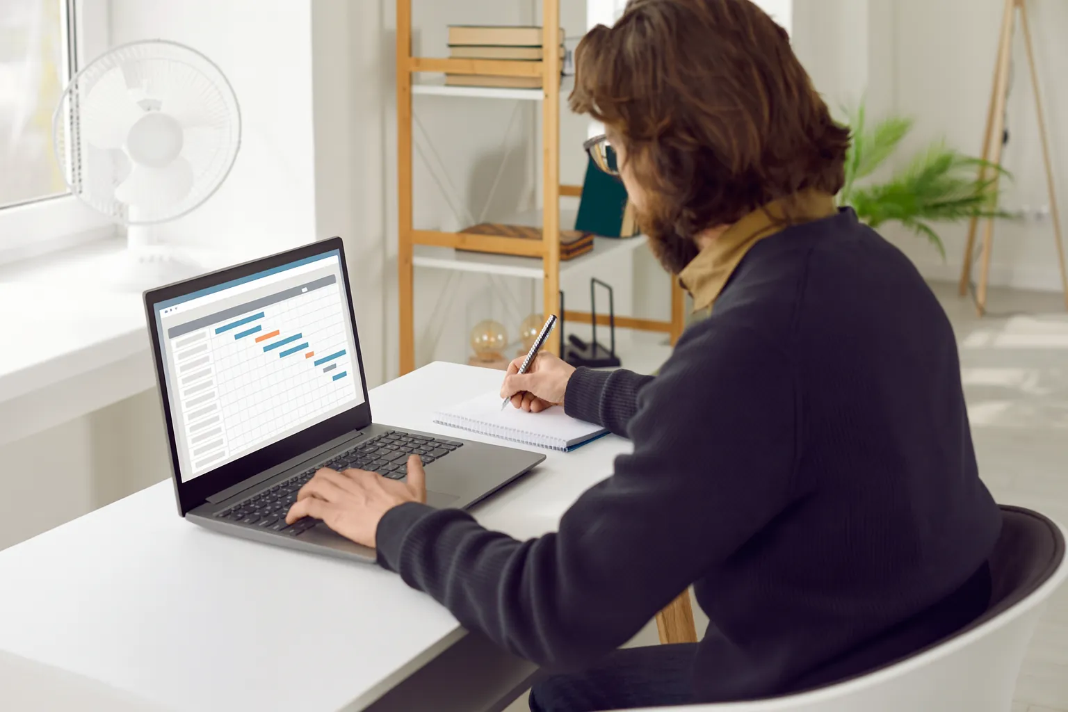 Pessoa usando notebook com diagrama de Gantt e anotando informações para organizar o checklist de anteprojeto.