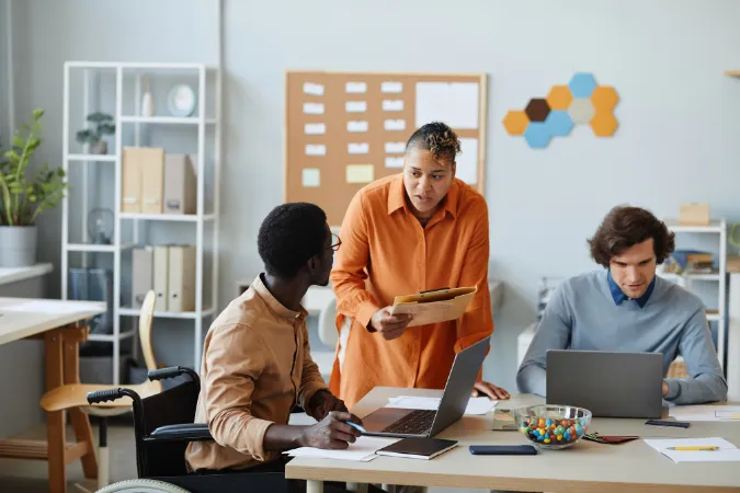 Equipe em ambiente de trabalho colaborativo conversando sobre tarefas, com quadro de gestão ao fundo