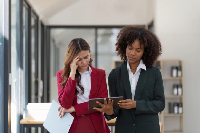 Duas mulheres analisando informações no tablet, com expressão de preocupação no ambiente corporativo.