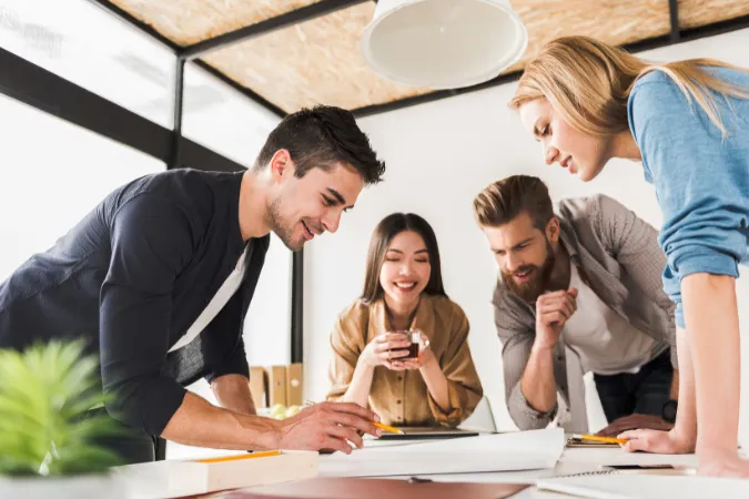 Time multidisciplinar colaborando em torno de uma mesa para definir etapas de projeto com base em planejamento reverso