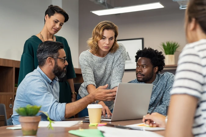 Grupo de profissionais discutindo entregas e prioridades em frente a um notebook.