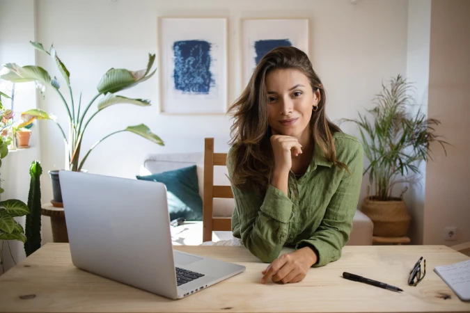 Mulher trabalhando em home office com laptop e anotações organizadas na mesa.