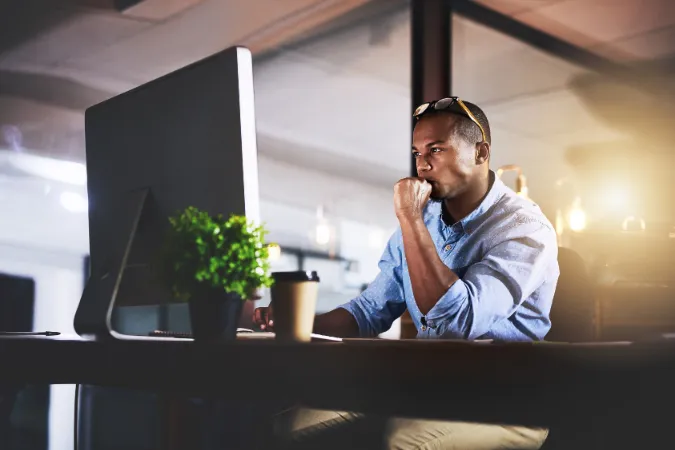 Homem concentrado diante do computador em ambiente noturno de trabalho