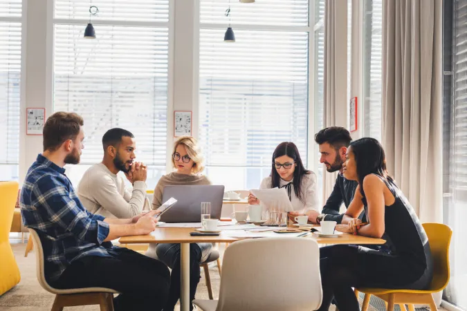Equipe multidisciplinar discutindo tarefas e metas em mesa de trabalho.