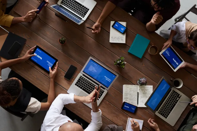 Profissionais utilizando notebooks e tablets com dashboards digitais em uma reunião de equipe.
