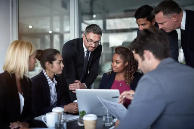 Grupo de executivos e gestores analisando cronograma de entregas em reunião corporativa.