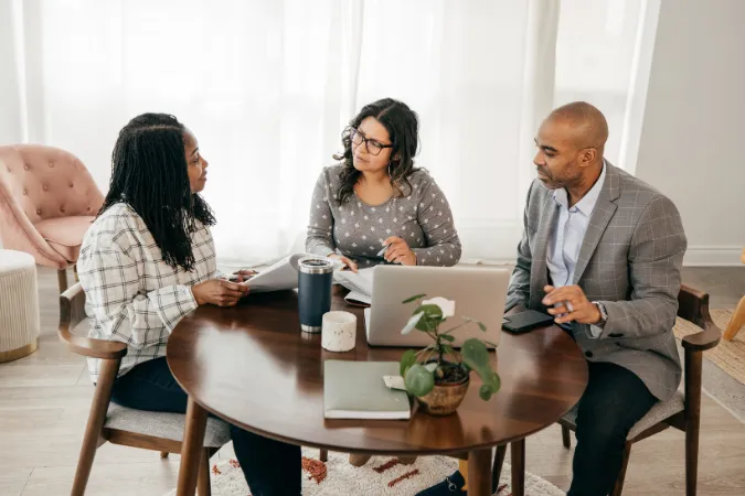 Equipe reunida em mesa de trabalho revisando entregáveis essenciais de consultoria, com notebook, documentos e discussão colaborativa para validação de decisões do projeto.