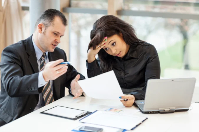 Profissionais analisando documentos com expressões de preocupação, ilustrando falhas de comunicação e falta de alinhamento na gestão de projetos.