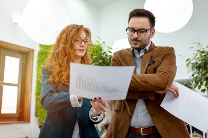 Profissionais avaliando gráficos e relatórios impressos, representando a importância de dados e indicadores na gestão de projetos.