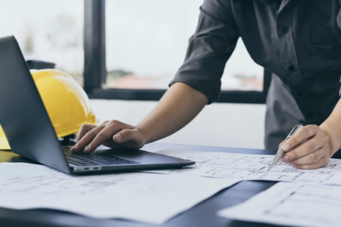 Profissional de engenharia utilizando notebook para gerenciar escopo, cronograma e orçamento do projeto.