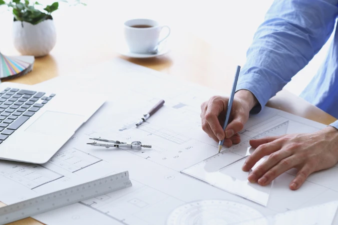 Profissional revisando desenhos técnicos e realizando ajustes em projeto arquitetônico durante etapa de validação.