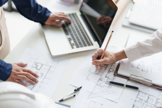 Arquitetos analisando plantas e fazendo anotações para organizar revisões e aprovações do projeto.