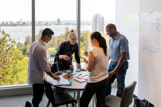 Equipe em reunião em pé ao redor de uma mesa, discutindo prioridades e próximos passos de um projeto ágil