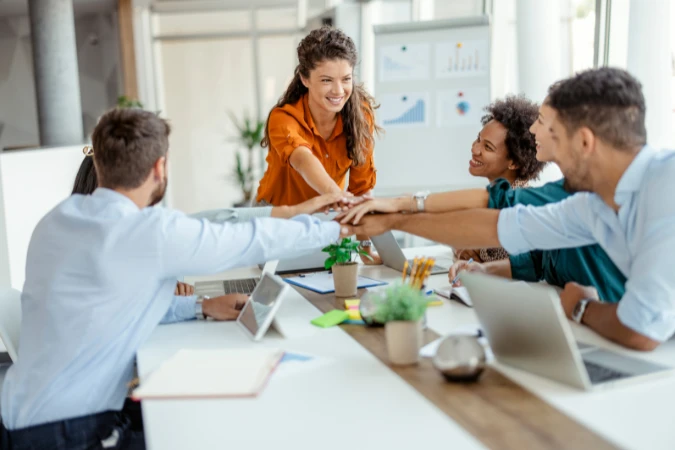 Equipe reunida colocando as mãos juntas como sinal de colaboração e alinhamento em um ambiente de trabalho