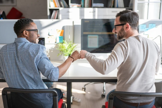 Dois profissionais em escritório trocando cumprimento, representando colaboração e alinhamento de equipe