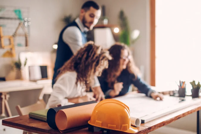 Equipe analisando plantas e cronograma de projeto, destacando planejamento estruturado e trabalho em equipe.