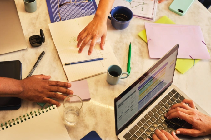 Equipe colaborando no planejamento de projetos usando software de gestão em laptop e materiais de organização