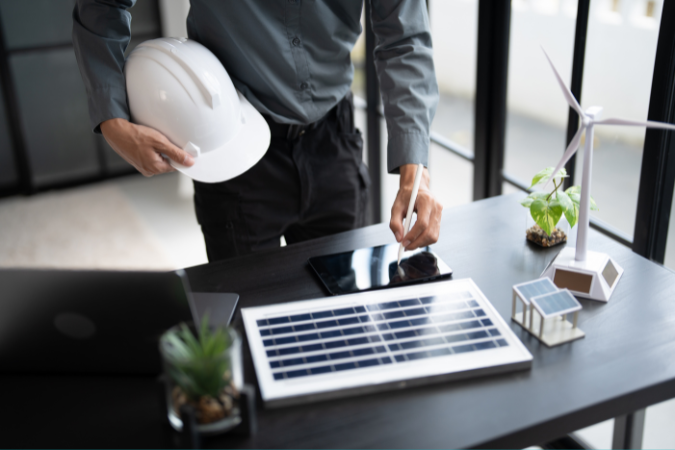 Engenheiro analisando painel solar e modelo de energia sustentável em mesa de trabalho com tablet e capacete de obra