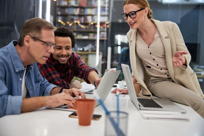 Profissionais colaborando em laptops em ambiente de trabalho para troca de conhecimento e redução da dependência de especialistas