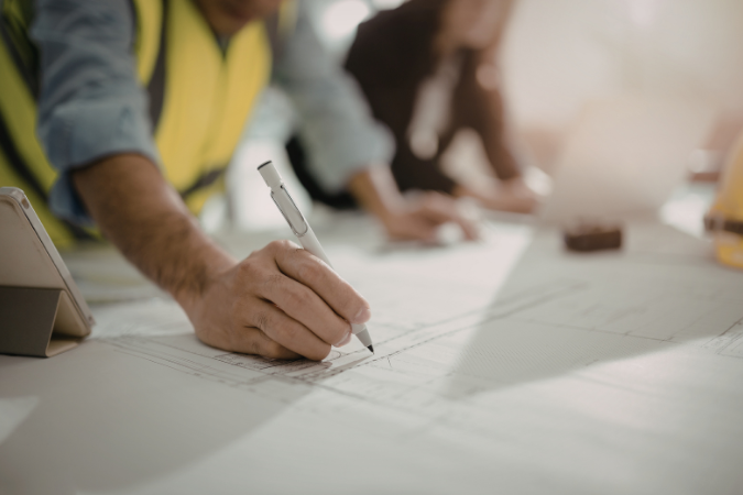 Profissional de engenharia marcando ajustes em planta técnica durante revisão de projeto arquitetônico