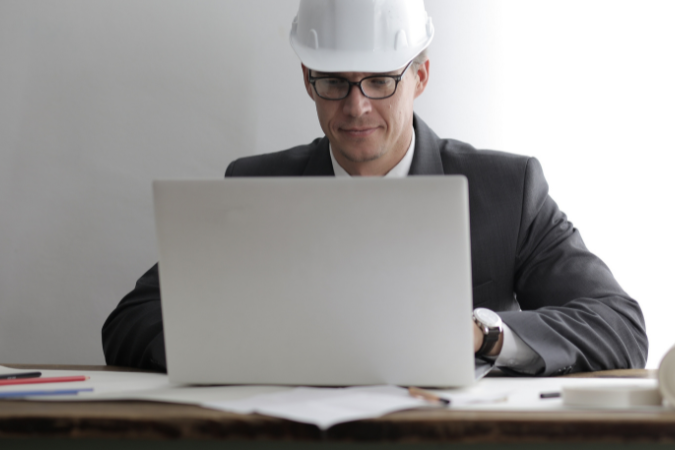 Engenheiro utilizando computador para acompanhar gestão de projetos e revisão técnica de obra
