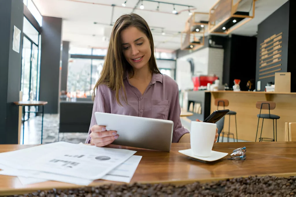 Mulher PMO de negócios trabalhando em um café em seu tablet enquanto bebe café
