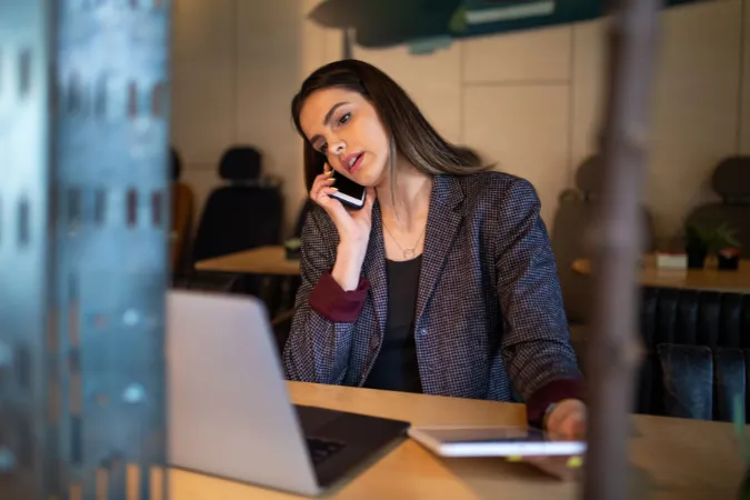 Profissional ao telefone com expressão de preocupação enquanto usa o notebook e anota em um caderno
