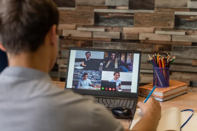 Homem participando de reunião virtual com quatro colegas via videoconferência no notebook.