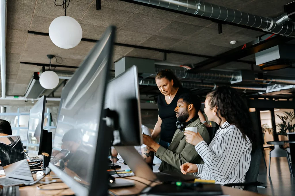 Male programmer discussing with female colleagues while sitting at desk in office