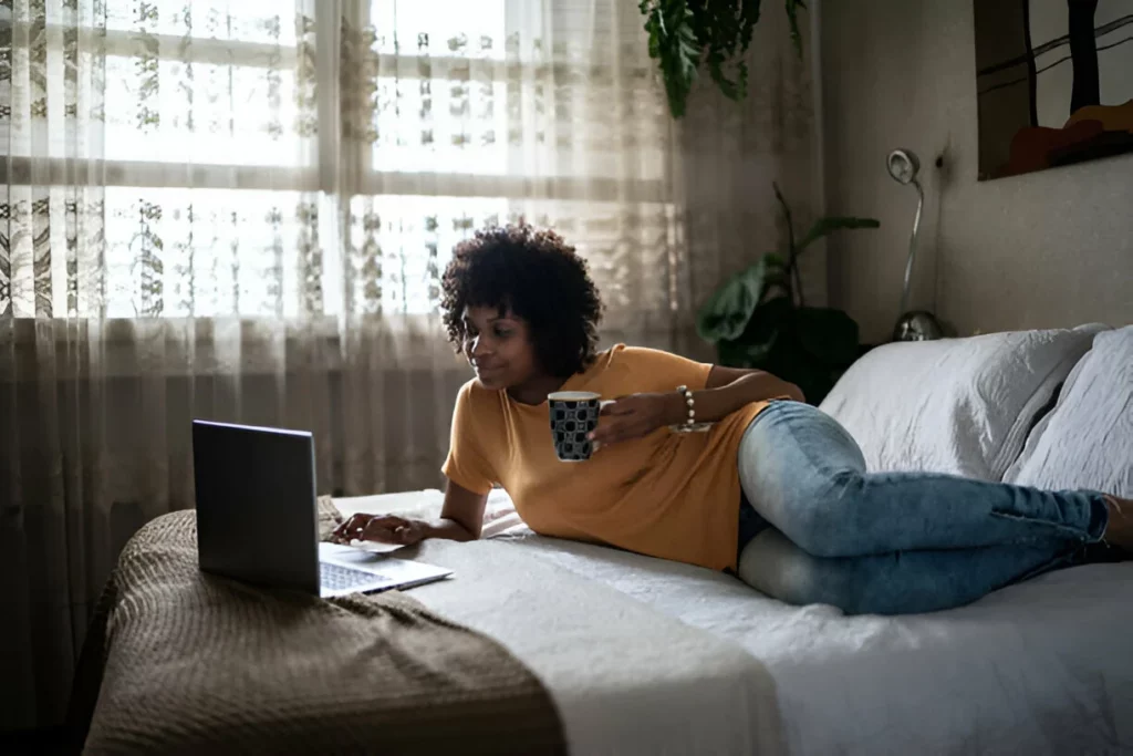 Jovem procrastinando com o laptop na cama em casa