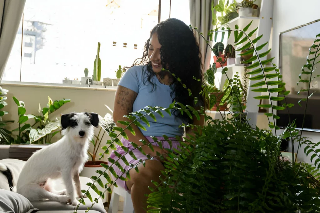 Jovem mulher negra cuidando de suas plantas em casa, enquanto seu animal de estimação observa