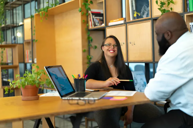 Duas pessoas em reunião de trabalho em um ambiente moderno, com laptop aberto e documentos sobre a mesa, representando colaboração e uso de tecnologia na gestão empresarial.
