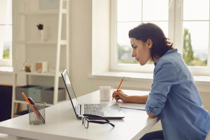 Mulher trabalhando concentrada em um notebook, com anotações e gráficos, representando os benefícios do ERP online na organização da gestão empresarial.