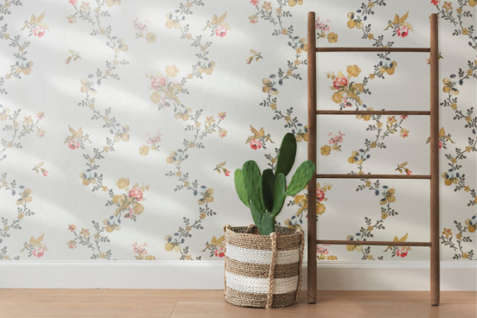 Ambiente com parede de papel de parede floral, com desenhos delicados de flores amarelas e rosas sobre fundo claro, acompanhado por uma escada de madeira decorativa e vaso com cacto.