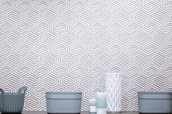 Parede decorada com papel de parede de padrão geométrico em tons claros, com prateleira exibindo cestos e vasos em azul e branco, criando um ambiente minimalista.