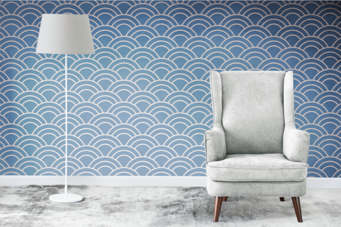 Sala com parede revestida de papel de parede azul com padrão de ondas em semicírculos dourados, acompanhada por poltrona cinza clara e luminária branca de chão.