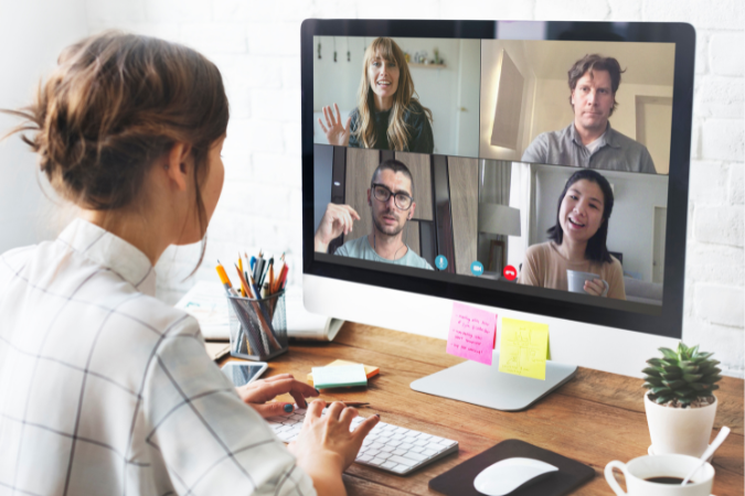 Mulher participando de reunião remota com quatro colegas, utilizando computador desktop em home office.