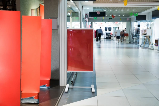 Fachada de loja em shopping com placas vermelhas chamativas posicionadas na entrada, destacando visualmente a comunicação promocional do espaço comercial